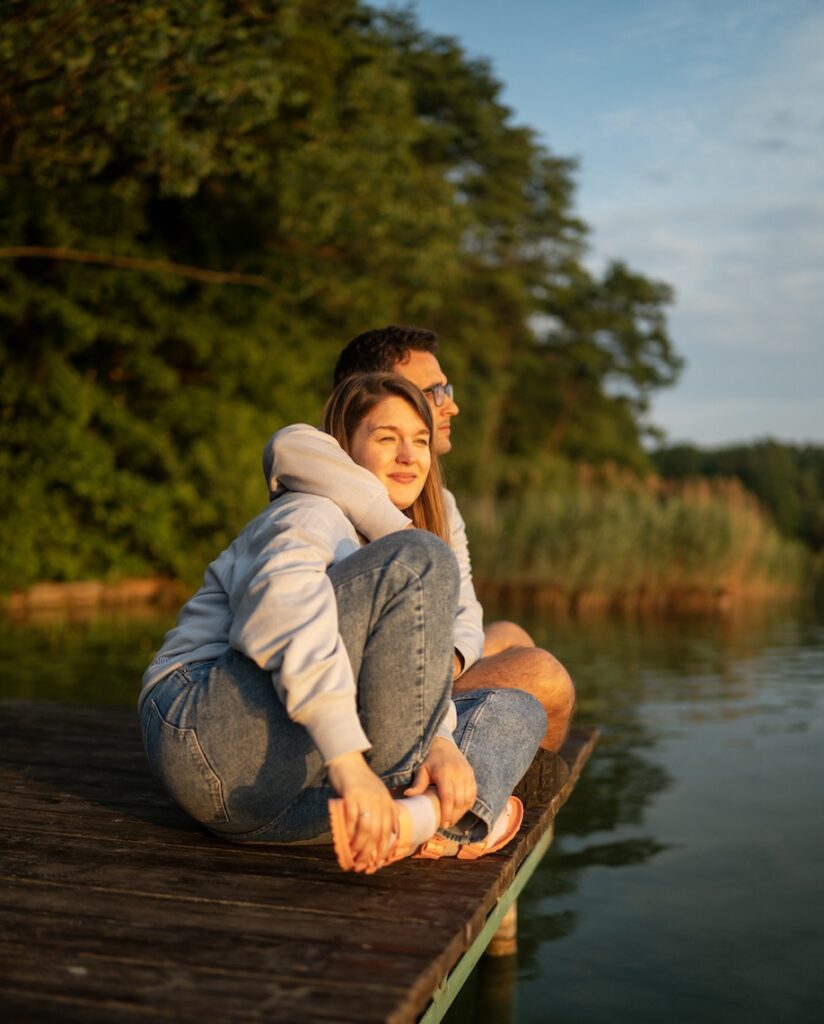 Romantic heterosexual couple embracing on a pier. Watching beautiful setting sun over water