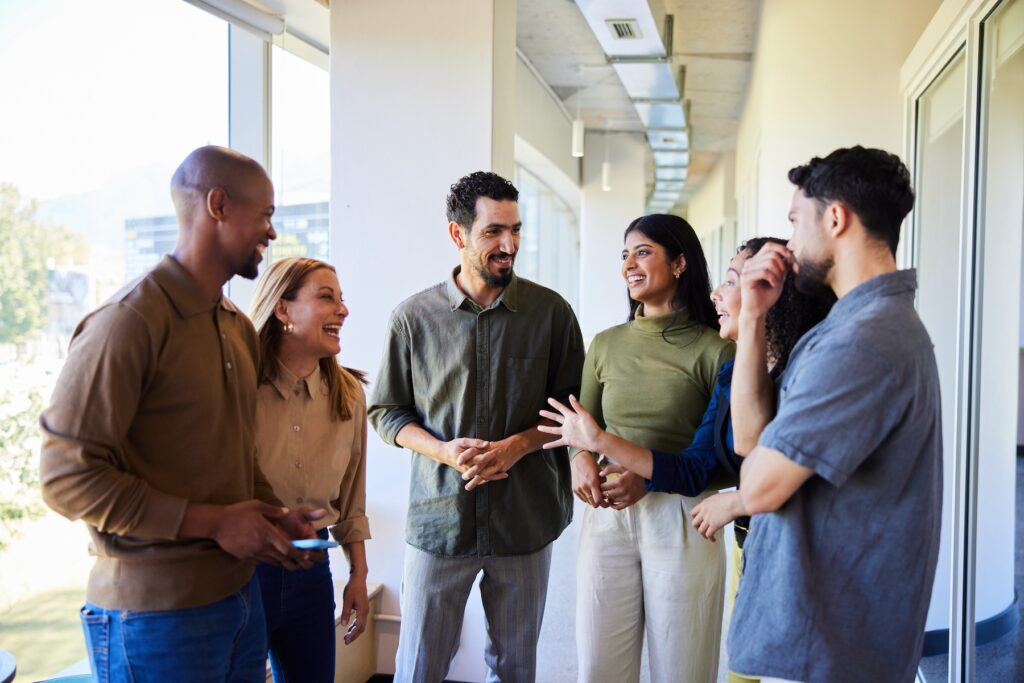 Diverse group of businesspeople talking and laughing while standing together in the corridor of an office