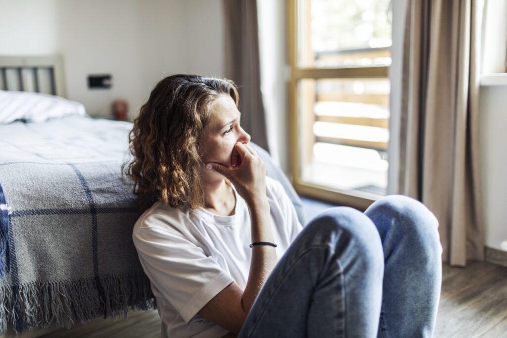 Young adult woman with depression sitting at home alone