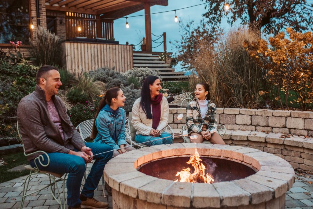 Family roasting marshmallows over open flame, campfire on backyard. Outdoor activity.