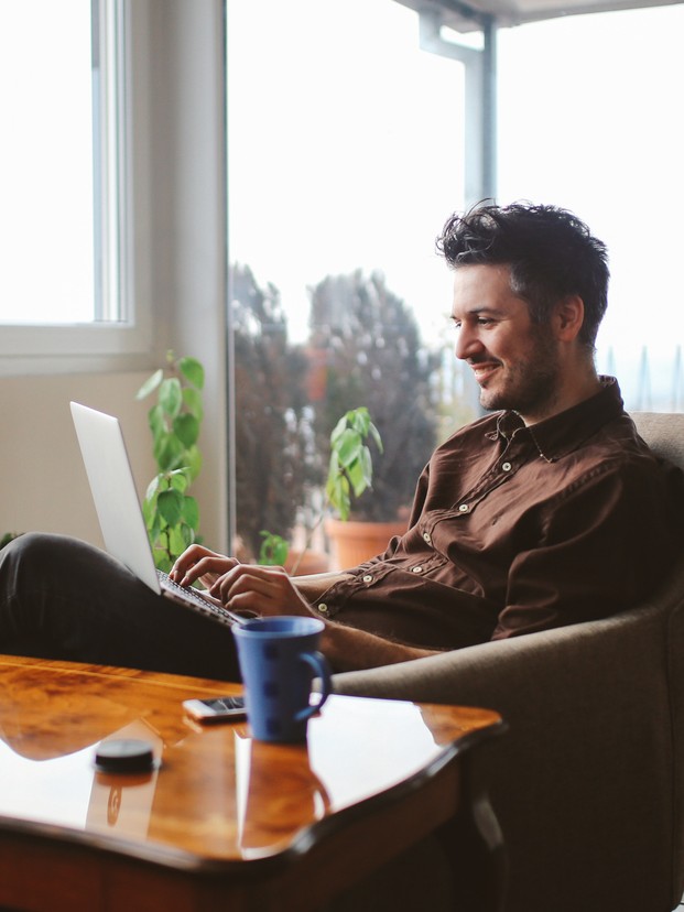Vintage toned portrait of a young man working at the table in the bright and beautiful apartment on the high floor in Belgrade, Serbia. He is wearing casual, everyday clothes, a brown shirt, and having a cup of coffee as well.